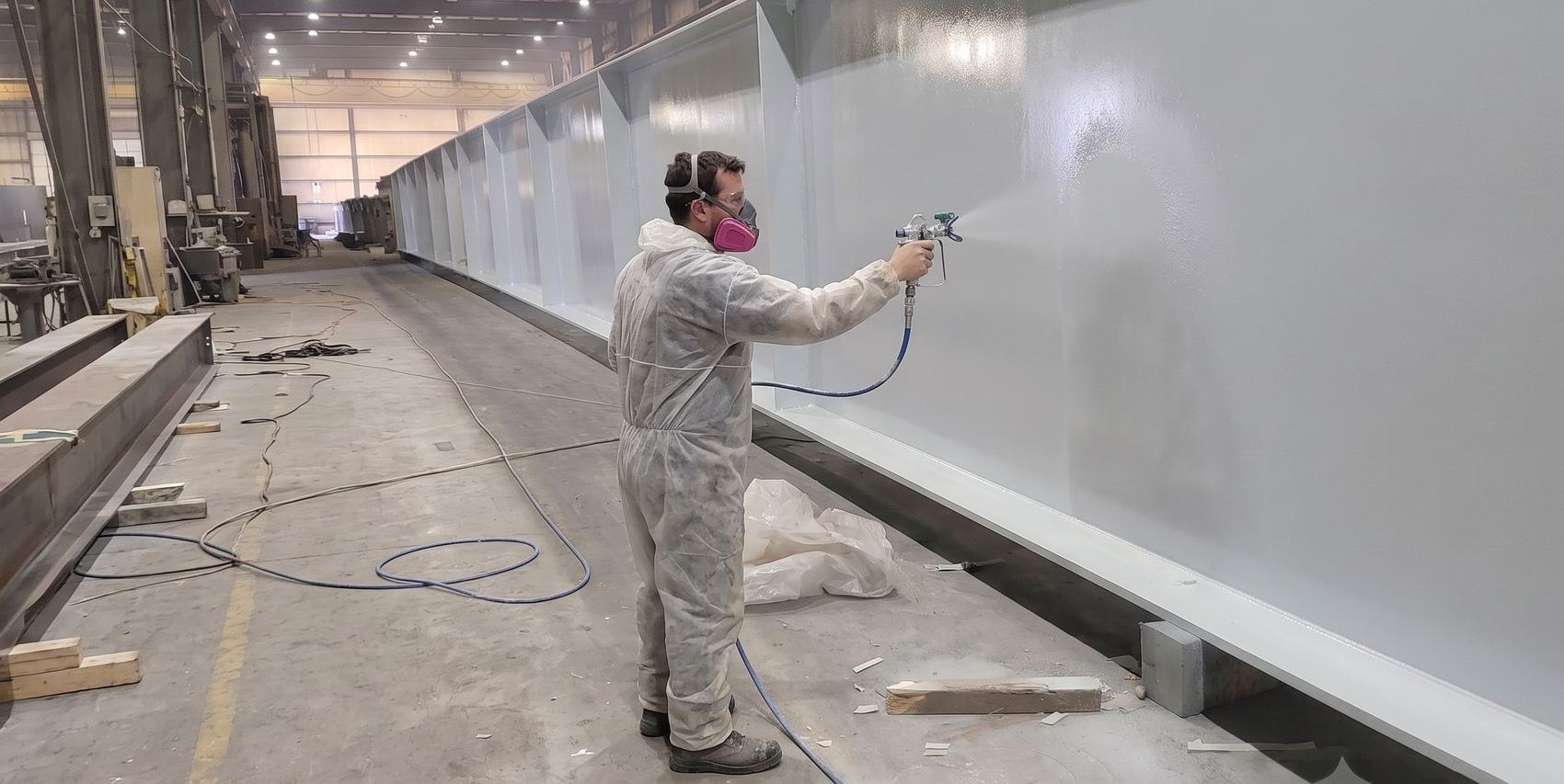 Applicator spray applying a finish coat to a fabricated structural steel girder inside the Regal Industrial shop